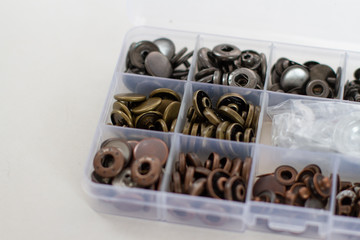 set of metal buttons for clothes in a plastic container on a white background