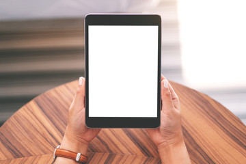 Top view mockup image of a woman sitting and holding black tablet pc with blank white desktop screen on wooden table