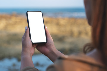 Mockup image of woman holding black mobile phone with blank desktop screen by the beach and sea