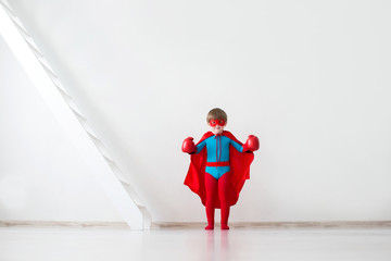 Little boy dreamer in a superhero costume and boxing gloves.