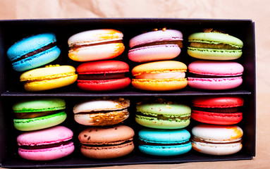 Tasty different colored macarons in black box on light background