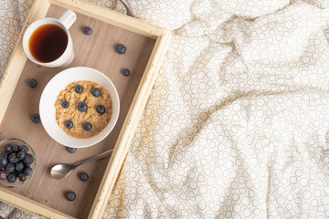 Oatmeal with berries on a tray in bed with tea, morning breakfast and mood. flat lay