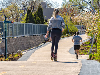 A woman is rollerblading riding skates and a man is jogging on The 606 Bloomingdale Train in Humboldt Park. Streets of Chicago, main streets in Illinois.
