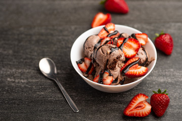 chocolate ice cream with strawberries on a dark background with a spoon, summer mood