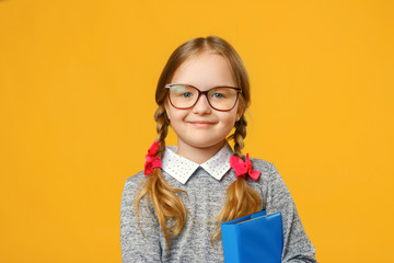 Closeup little girl schoolgirl on yellow background. The child is holding a book. The concept of...