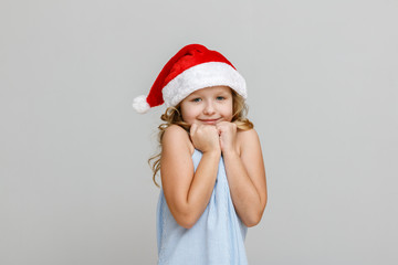 Portrait of a happy smiling little blonde girl on a gray background. Child in santa hat. Christmas celebration concept