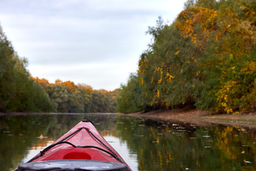 Red kayak sailing down a river on a sunny autumn day against yellow foliage trees reflected in the water