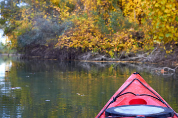 Bow of red kayak on river at calm autumn day. View on river from the bow of kayak. Autumn kayaking