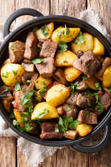 fried pork with potatoes and mushrooms closeup in the pan. Vertical top view