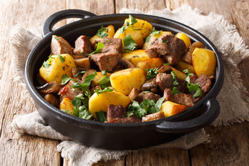 Simple hearty meal of fried potatoes with pork meat and mushrooms close-up in a pan. horizontal