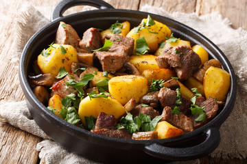 Traditional fried potatoes with pork and mushrooms close-up in a pan on the table. horizontal