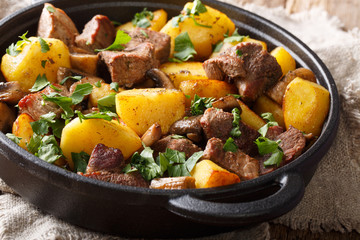 Homemade food of fried pork with potatoes and mushrooms close-up in a frying pan. horizontal