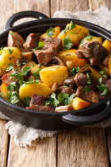 Rustic style fried pork with potatoes and mushrooms close-up in a pan. vertical