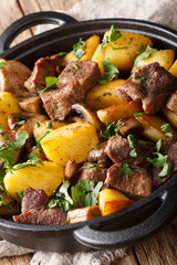fried pork with potatoes and mushrooms closeup in the pan. vertical