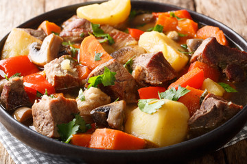 Tasty thick stew pork with mushrooms, potatoes, carrots and peppers closeup on a plate. horizontal