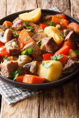 pork stew with mushrooms, potatoes, carrots and peppers close-up on a plate. vertical
