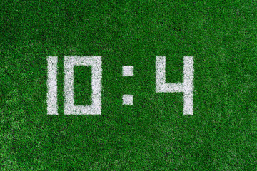 Football score.White numbers ten and four are drawn on the green grass,creative scoreboard