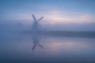 Naklejka na ściany i meble Windmill 'de Witte Molen' reflected in the canal during a foggy dawn in Holland.