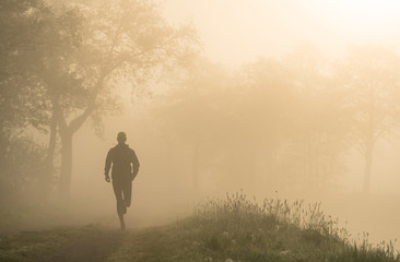Athlete running on a gravel road during a foggy, spring sunrise in the countryside.