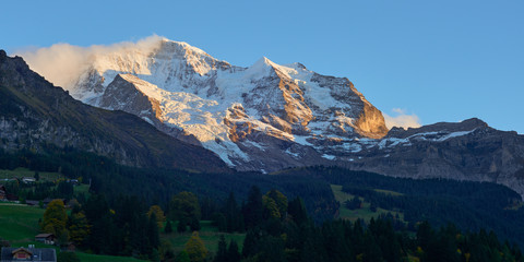 Panoramic view of the Jungfrau high mountain peak in the clouds above Swiss Alpine village Wengen at sunset.