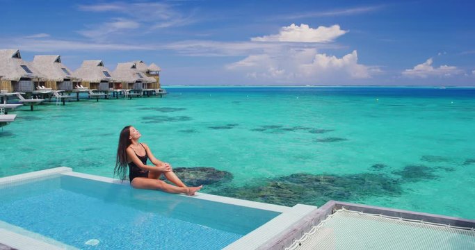 Summer Vacation Woman in bikini in luxury swimming pool in overwater bungalow. Elegant lady relaxing sunbathing enjoying travel holidays at resort pool. Skin and beauty care lifestyle.