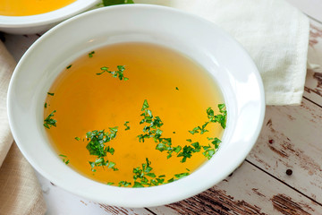 Cooked hot bone broth with spices and fresh herbs. Medical dietary broth and superfood. For ketogenic diet and paleo diet. Serve on an individual plate on a wooden background and with a white napkin.