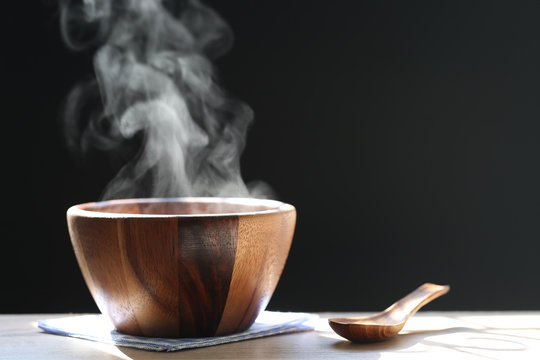 Selective focus of smoke rising with hot soup in cup on dark background
