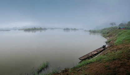 River view misty morning beside the bank of a small fishing boat floating in Mekong river around with soft fog in the sky background, Ban Muang, Sang Khom District, Nong Khai, Thailand.