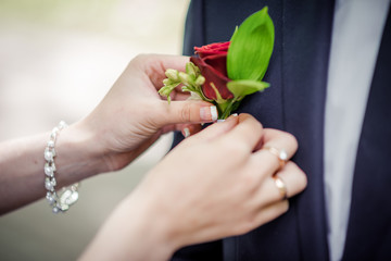 At the wedding, the bride straightens the flower in the outer pocket of the groom's jacket. Close-up.