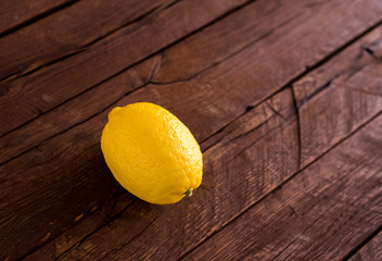 Single yellow lemon on brown oak wooden boards. Warm colours, natural light.