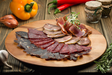 Cured meat in a wooden plate on a wooden table with vegetables
