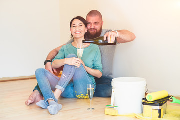 Happy couple drinking champagne celebrating new home - housewarming, painting and renovation concept
