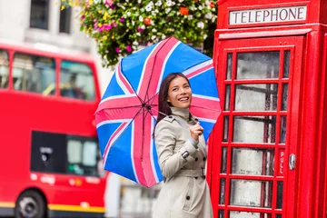 Muurstickers Londense toeristische reisvrouw met Britse vlagparaplu, telefooncel, rode grote bus. Europa reisbestemming Aziatisch meisje met Britse iconen, rode telefooncel, dubbeldekker hop on hop off bus in beroemde stad. © Maridav