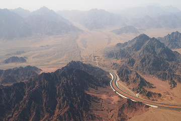 Aerial view of a highway road curving between treeless rocky mountains and desert on the south of Sinai Peninsula near Sharm El Sheikh