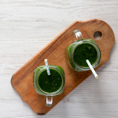 Glass jars full of green smoothie with spinach, avocado and banana over white wooden background....