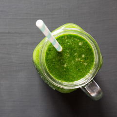 Glass jar full of green smoothie with spinach, avocado and banana over black background, top view. Flat lay, overhead, from above.