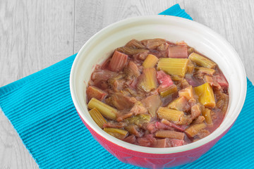 Rhubarb stewed in a mixing bowl on a blue placemat with a grey wood background