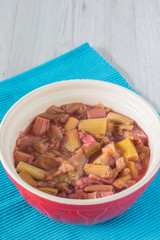 Rhubarb stewed in a mixing bowl on a blue placemat with a grey wood background