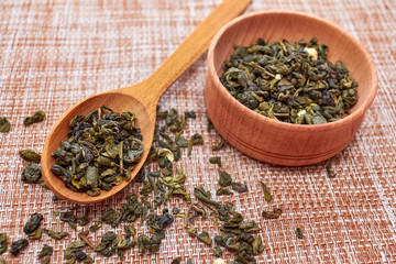 The composition of natural tea with jasmine. A macro photo of tea petals on a wooden spoon with jasmine. Tea with jasmine flowers ingredients located on a wooden board. Green tea in a wooden bowl.