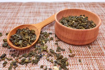 The composition of natural tea with jasmine. A macro photo of tea petals on a wooden spoon with jasmine. Tea with jasmine flowers ingredients located on a wooden board. Green tea in a wooden bowl.