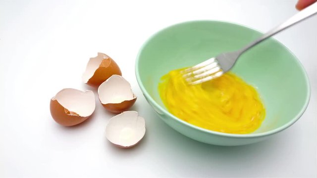 Slide shot of Beating the egg yolk with fork in the green bowl isolated on white background