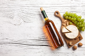 White wine bottle, grape, honey, nuts and cheese on white wooden board
