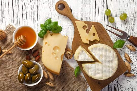 Cheese, grape, honey and nuts on white wooden table