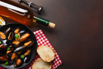 Seafood mussels and basil leaves in a black plate with wine bottle and corkscrew on towel and rusty background