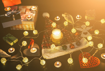 Candles burning among beautiful Christmas lights and garland. New Year festive background. Presents, gifts, greeting postcard for winter holidays.