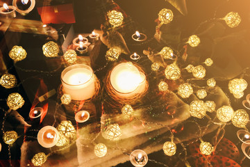 Candles burning among beautiful Christmas lights and garland. New Year festive background. Presents, gifts, greeting postcard for winter holidays.