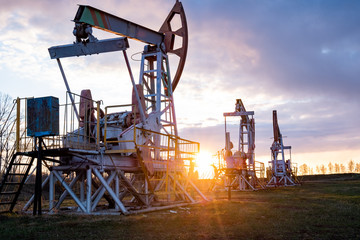 Naklejka premium Oil well at sunset. Oil production by a rocker at sunset. Rocking machine for oil