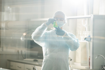 Serious busy young female chemist in protective goggles and mask doing laboratory testing for...