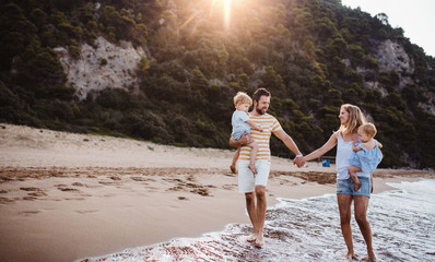A family with two toddler children walking on beach on summer holiday at sunset.