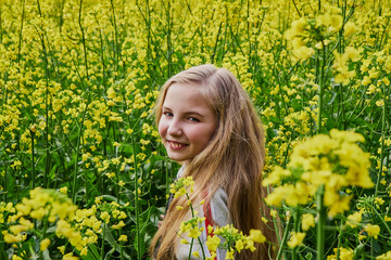 Naklejka na ściany i meble Closeup young girl happy on a sunny day in a rapeseed field, mustard with lots of yellow flowers